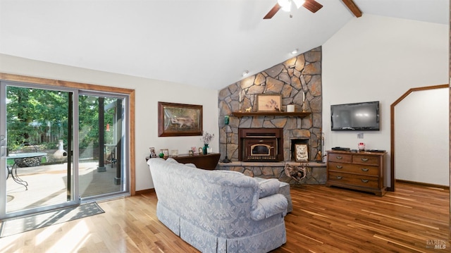 living room featuring beam ceiling, a ceiling fan, wood finished floors, a stone fireplace, and baseboards