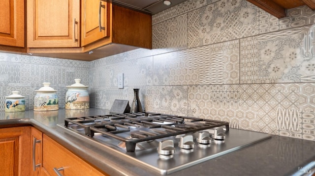 details featuring decorative backsplash, extractor fan, brown cabinetry, and stainless steel gas cooktop