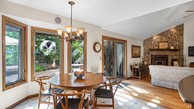 dining space featuring light wood finished floors, baseboards, lofted ceiling, a fireplace, and a notable chandelier