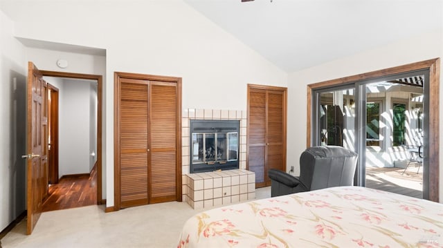 bedroom featuring high vaulted ceiling, a tile fireplace, access to exterior, light colored carpet, and two closets