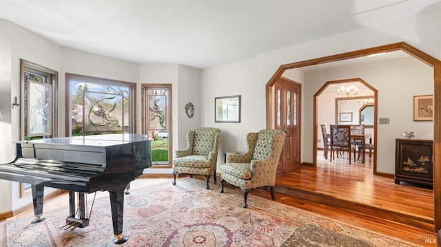 living area with arched walkways, a notable chandelier, baseboards, and light wood-style floors