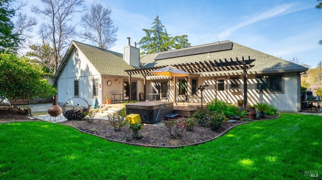 rear view of property featuring a chimney, a hot tub, a yard, and a pergola