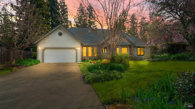 view of front of house with a garage, stone siding, a lawn, and driveway