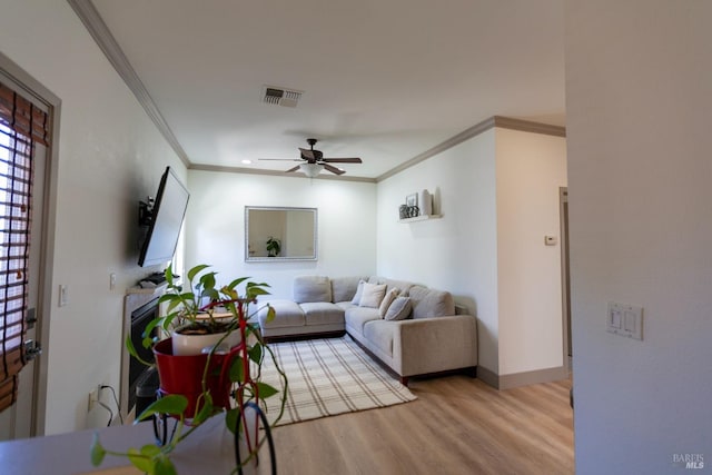 living area featuring a ceiling fan, baseboards, wood finished floors, visible vents, and ornamental molding