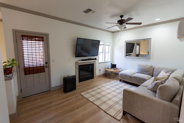 living area with visible vents, wood finished floors, a glass covered fireplace, crown molding, and baseboards