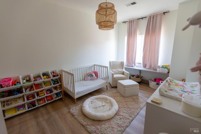 bedroom featuring visible vents, a crib, and wood finished floors