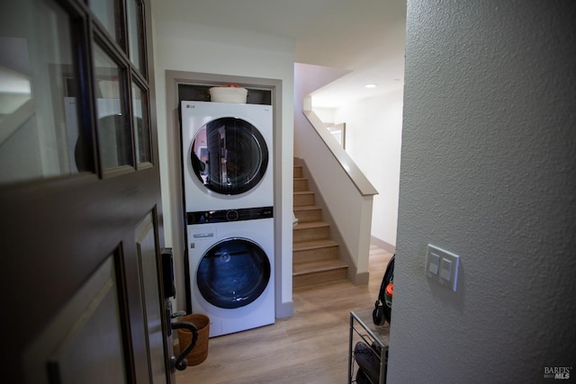 laundry room featuring stacked washer / dryer, laundry area, light wood-style floors, and a textured wall