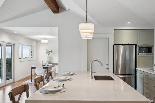 kitchen with a center island with sink, light wood finished floors, vaulted ceiling with beams, a sink, and stainless steel appliances