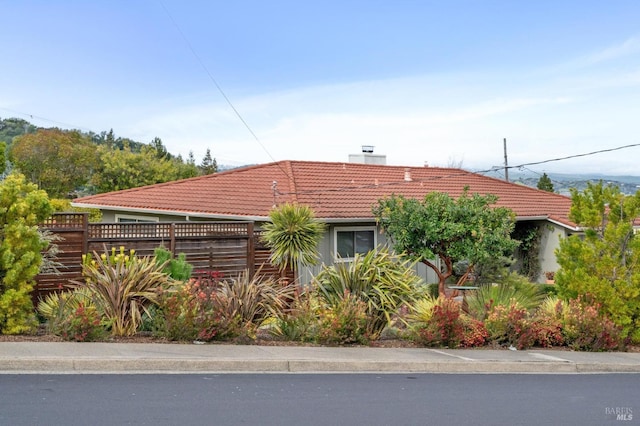 view of front of house with a tiled roof, a chimney, and fence