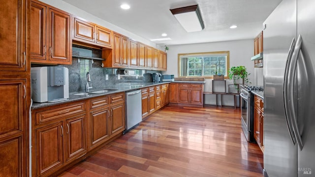 kitchen with a sink, wood finished floors, stainless steel appliances, brown cabinetry, and decorative backsplash