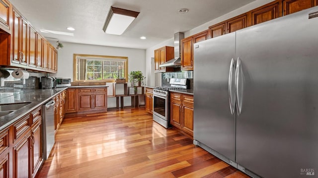 kitchen with brown cabinets, light wood-type flooring, stainless steel appliances, wall chimney exhaust hood, and tasteful backsplash