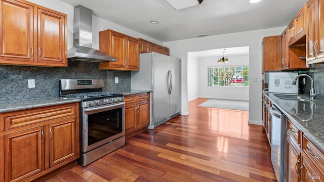 kitchen with dark wood-style floors, visible vents, appliances with stainless steel finishes, wall chimney range hood, and brown cabinets