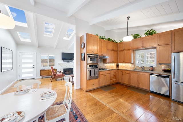 kitchen with tasteful backsplash, under cabinet range hood, light wood-style floors, stainless steel appliances, and a sink