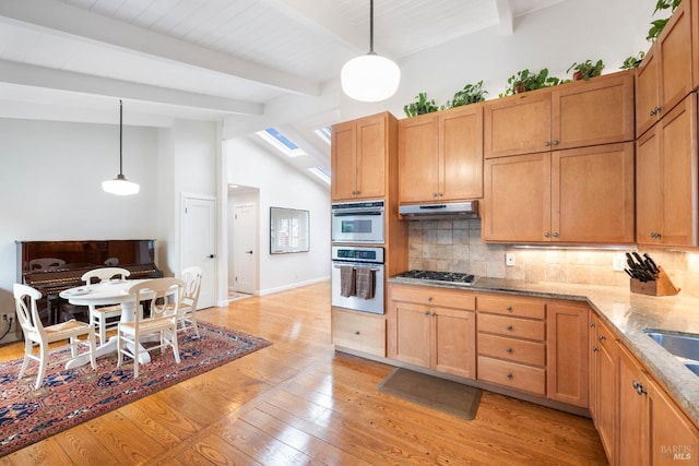 kitchen featuring under cabinet range hood, backsplash, stainless steel appliances, vaulted ceiling with skylight, and light wood-style floors