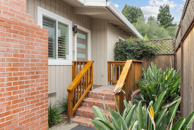 view of exterior entry featuring fence and brick siding