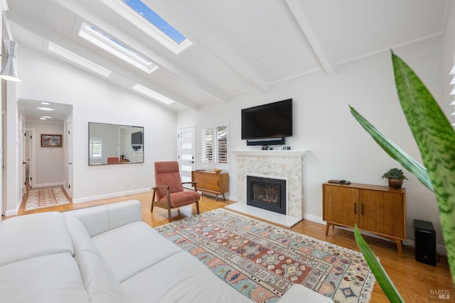 living area with a glass covered fireplace, vaulted ceiling with skylight, baseboards, and wood finished floors