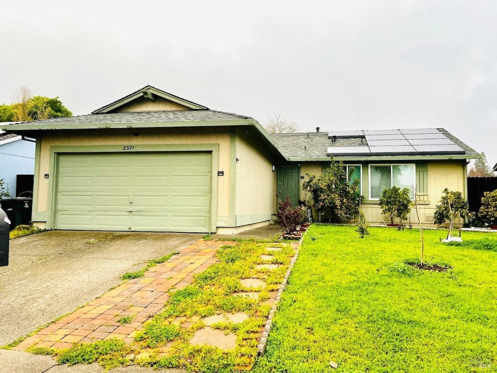 ranch-style house featuring driveway, solar panels, an attached garage, a shingled roof, and a front lawn