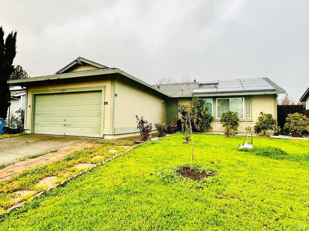 ranch-style home featuring solar panels, a front lawn, an attached garage, and concrete driveway