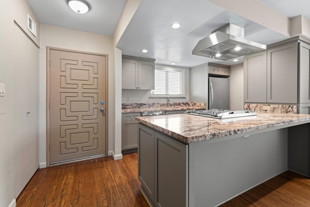 kitchen with a peninsula, dark wood-style flooring, gray cabinets, freestanding refrigerator, and exhaust hood