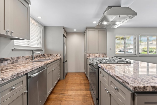 kitchen with light wood-style flooring, gray cabinets, a sink, appliances with stainless steel finishes, and wall chimney exhaust hood