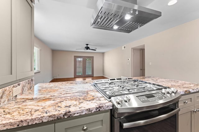 kitchen with light stone counters, gas range, wall chimney exhaust hood, and gray cabinets