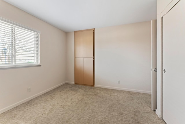 unfurnished bedroom featuring light carpet, a closet, and baseboards