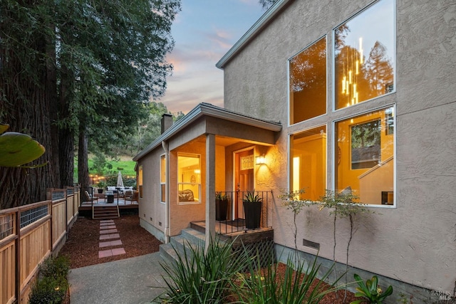 view of side of home featuring stucco siding, a chimney, and fence