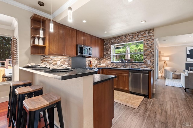 kitchen featuring dark countertops, backsplash, a peninsula, wood finished floors, and stainless steel appliances