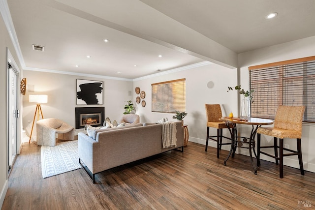 living area with wood finished floors, visible vents, baseboards, ornamental molding, and a glass covered fireplace