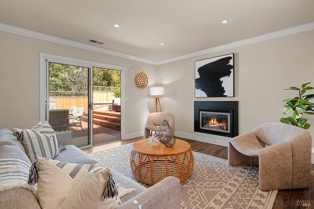 living room with a glass covered fireplace, wood finished floors, visible vents, and ornamental molding