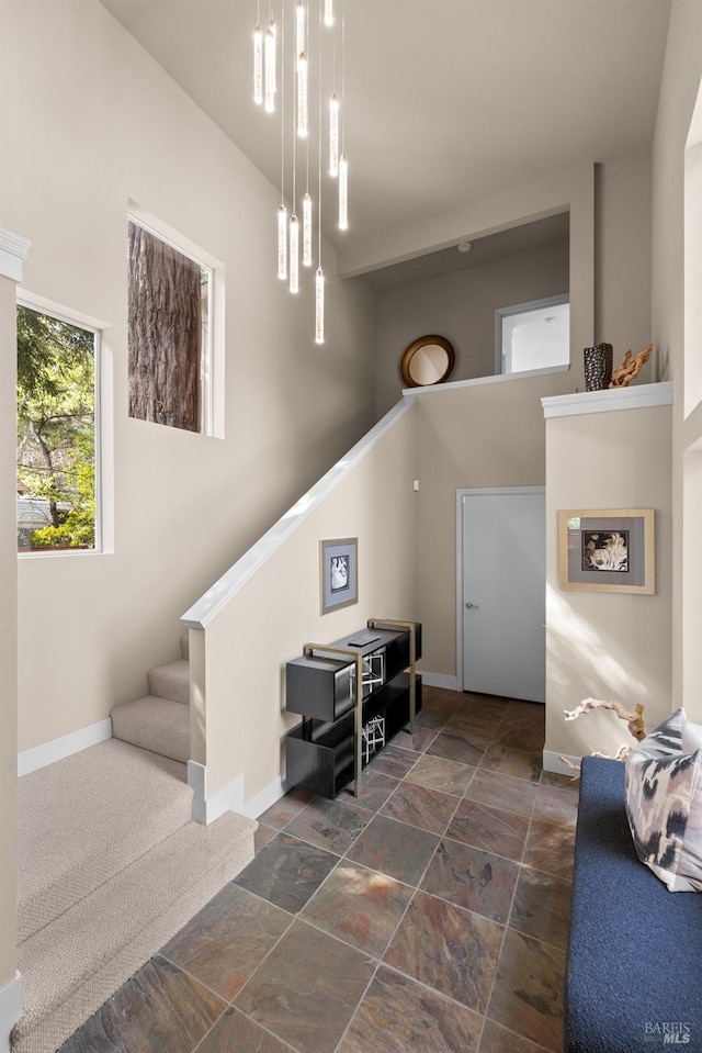 interior space featuring stone finish floor, stairs, baseboards, and a towering ceiling