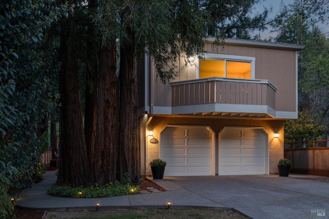 view of front of home with a garage, a balcony, concrete driveway, and fence