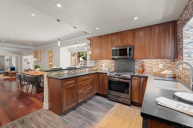 kitchen with a peninsula, wood finished floors, brown cabinetry, stainless steel appliances, and a sink