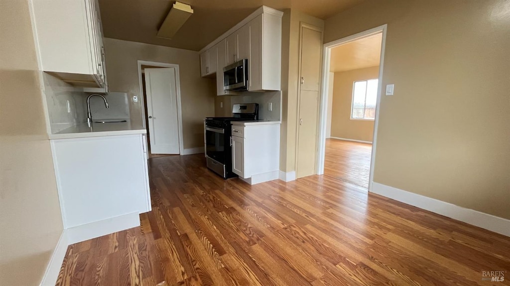 kitchen with a sink, stainless steel microwave, wood finished floors, gas stove, and white cabinets