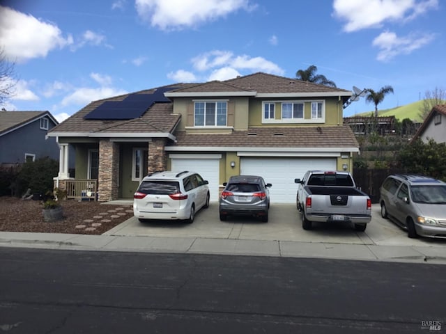 view of front of property with stone siding, an attached garage, concrete driveway, solar panels, and stucco siding