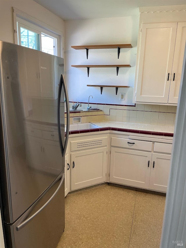 kitchen featuring tile countertops, light floors, freestanding refrigerator, white cabinets, and open shelves