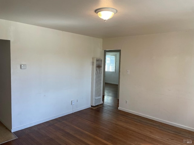 empty room with dark wood finished floors, a heating unit, and baseboards