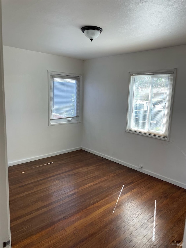 spare room with baseboards and dark wood-style floors