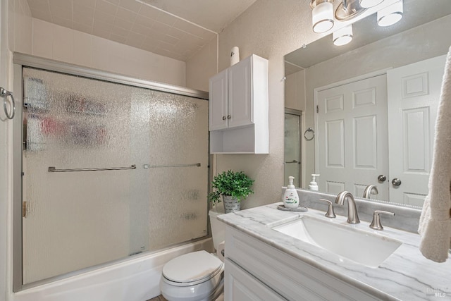 full bathroom with a textured wall, shower / bath combination with glass door, vanity, and toilet