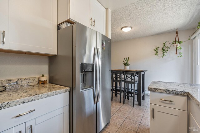 kitchen featuring light countertops, light tile patterned floors, white cabinets, stainless steel fridge, and a textured ceiling