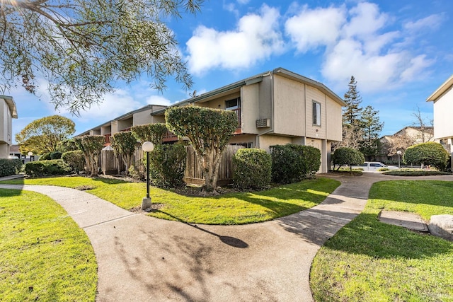 view of side of property featuring fence, stucco siding, a lawn, a garage, and driveway