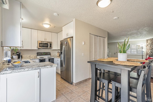 kitchen featuring light tile patterned floors, appliances with stainless steel finishes, white cabinets, and a sink