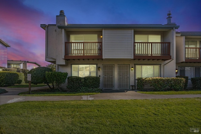 view of property with a front lawn, a balcony, and stucco siding