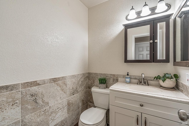 half bath with vanity, toilet, tile walls, and a textured wall