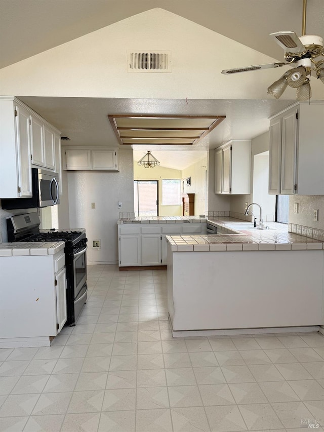 kitchen with visible vents, a sink, tile countertops, stainless steel appliances, and a peninsula