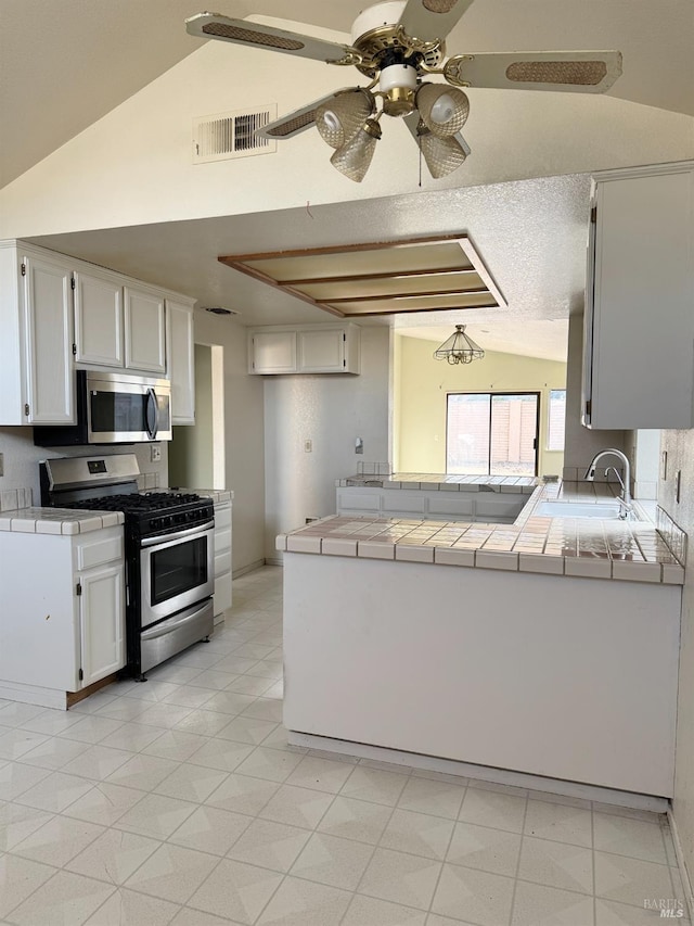 kitchen featuring visible vents, appliances with stainless steel finishes, lofted ceiling, and tile counters