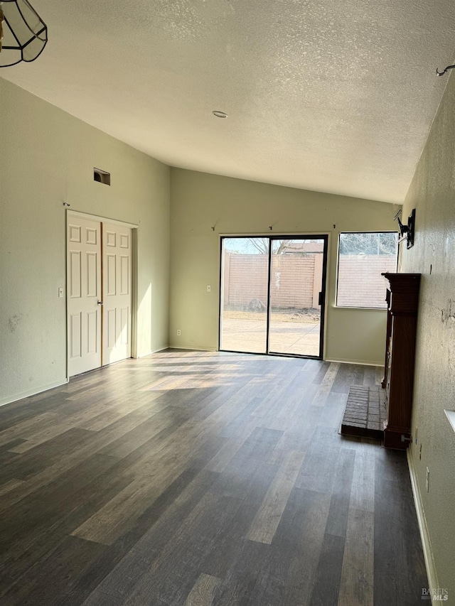 interior space with visible vents, a textured ceiling, wood finished floors, baseboards, and vaulted ceiling