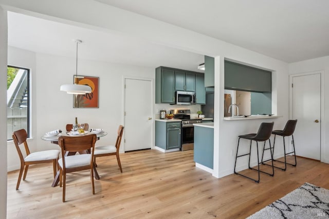 kitchen with light wood finished floors, pendant lighting, light countertops, appliances with stainless steel finishes, and green cabinetry