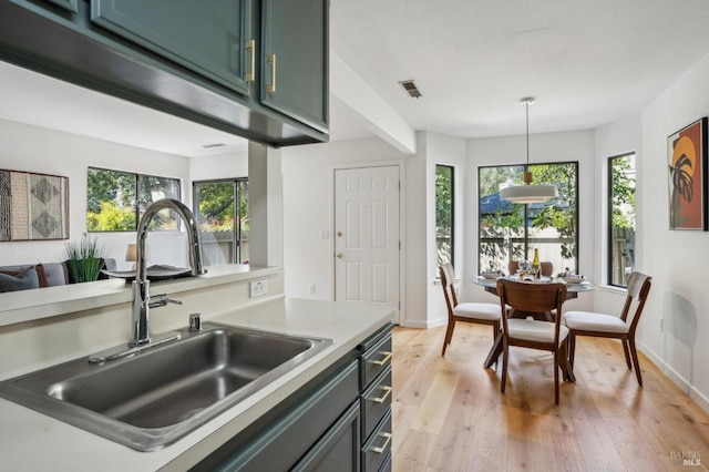 kitchen featuring hanging light fixtures, plenty of natural light, light wood finished floors, and a sink