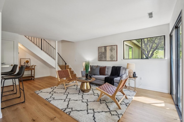 living room with stairway, visible vents, baseboards, and light wood-style floors